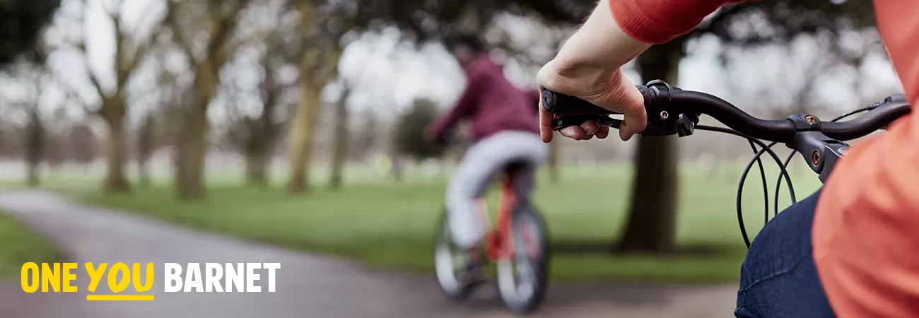 Two people cycling on a tarmac path through a park.